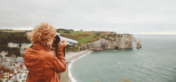 Rear view of woman looking at sea through coin-operated binoculars