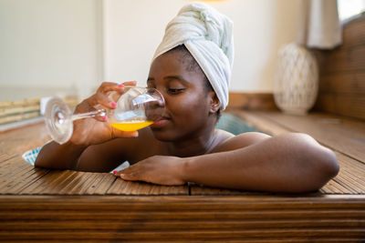 Black woman with a towel covering her head drinking a juice inside a jacuzzi