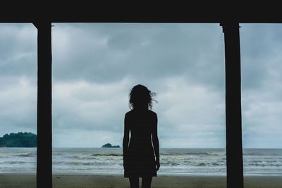 Rear view of woman standing at beach against sky