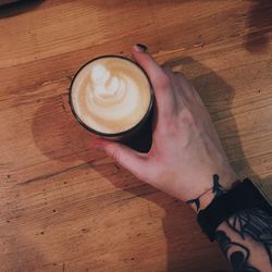 High angle view of hand holding coffee cup on table