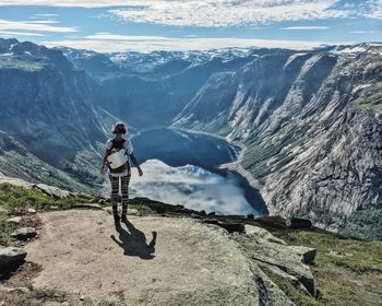 Rear view of woman standing on cliff by lake against mountains