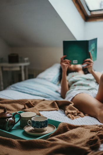 Woman reading book while lying on bed