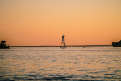 Silhouette lighthouse by sea against clear sky during sunset