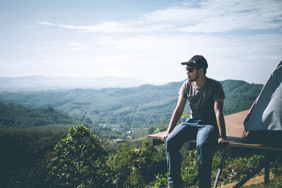 Man sitting on mountain against sky