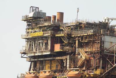 Low angle view of crane by building against clear sky