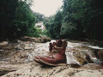 Shoes on rock against stream at forest