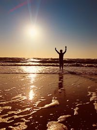 Silhouette person on beach against bright sun