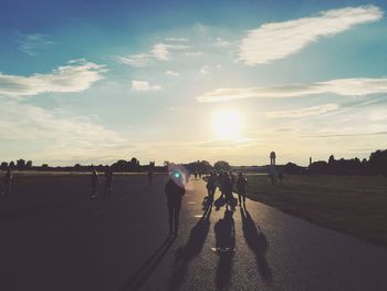 People walking on road against sky during sunset