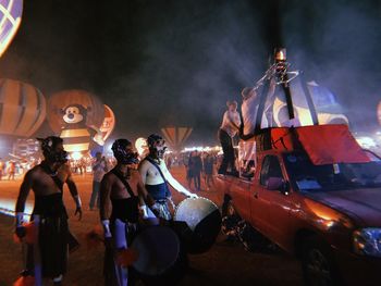 People on illuminated carousel against sky at night
