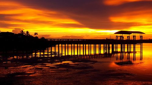 Silhouette pier over sea against orange sky