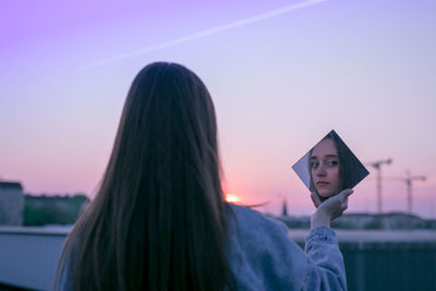 Woman holding mirror against sky during sunset