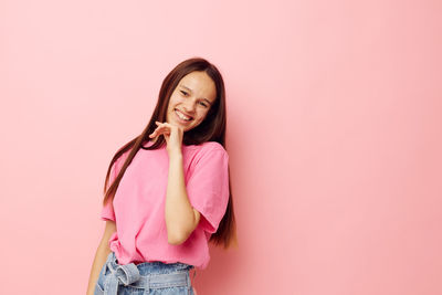 Portrait of young woman standing against pink background