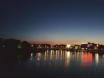 Illuminated buildings by river against sky at night