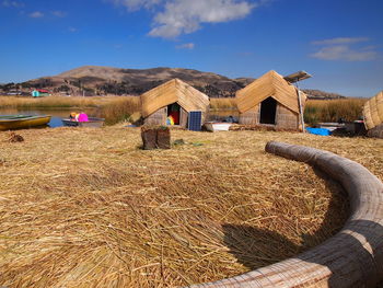 Hay bales on field by houses against sky