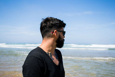 Young man wearing sunglasses on beach against sky