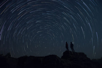Silhouette men standing on rocks against star trail at night