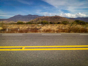 Yellow road by landscape against sky