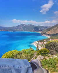 Low section of man sitting on mountain by sea against sky