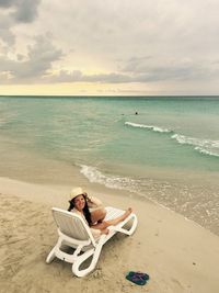 High angle portrait of cheerful woman sitting on chair at beach