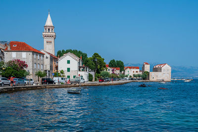 Buildings by sea against clear blue sky