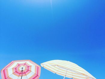 Low angle view of umbrellas against clear blue sky