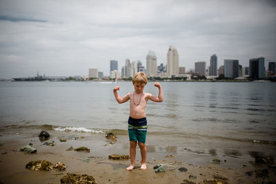 Full length of shirtless man standing at beach against sky