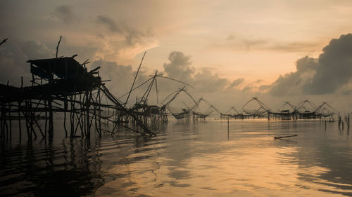 Silhouette fishing nets in sea against sky during sunset