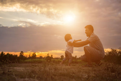 Father playing with daughter on land against sky during sunset