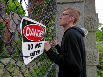 Side view of man standing by chainlink fence with do not enter sigh board