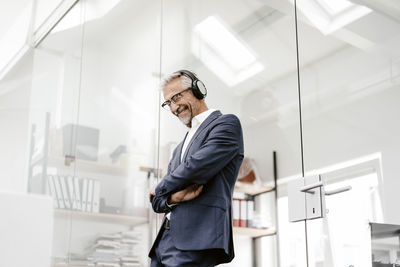 Happy mature businessman in office wearing headphones
