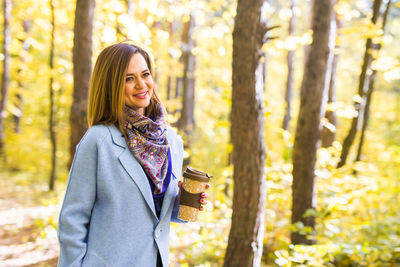 Portrait of young woman standing in forest during autumn