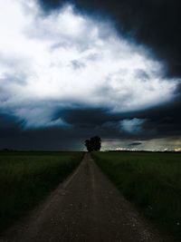 Road passing through field against cloudy sky