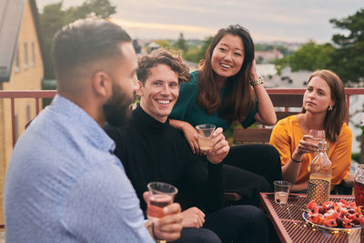 Cheerful friends enjoying social gathering on terrace during sunset