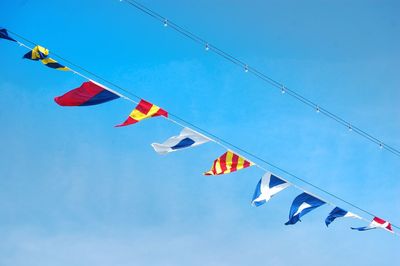 Low angle view of flags hanging against blue sky