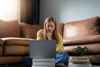 Portrait of woman using laptop while sitting on sofa at home