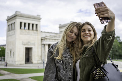 Young woman taking selfie with friend against built structure