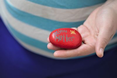 Midsection of woman holding red pebble with text