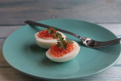 Red caviar with parsley lies on boiled and chopped eggs on a blue plate.	