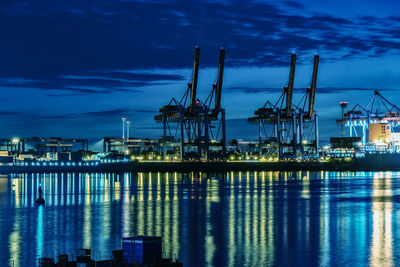 Illuminated city at harbor against sky during night