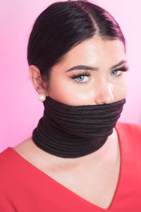 Portrait of young woman with tied mouth against pink background