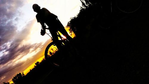 Low angle view of silhouette person riding bicycle against sky during sunset