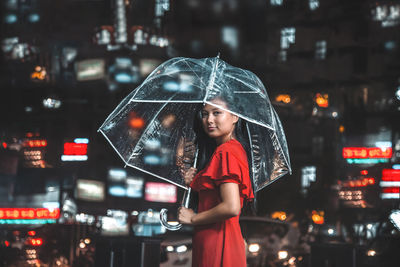 Woman standing on wet illuminated city during rainy season at night