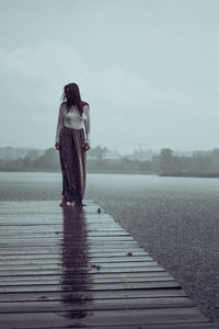 Full length of woman standing on pier by lake against sky