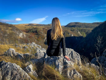 Rear view of woman standing on rock against sky