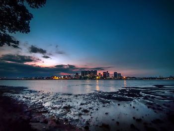 Scenic view of sea with urban skyline in background against sky at dusk