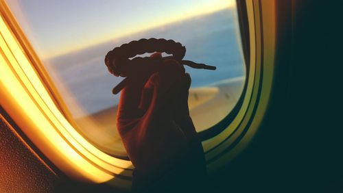 Cropped image of person holding bracelet against airplane window