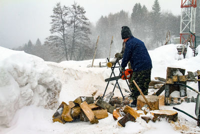 Side view of man cutting wood while standing on snow field