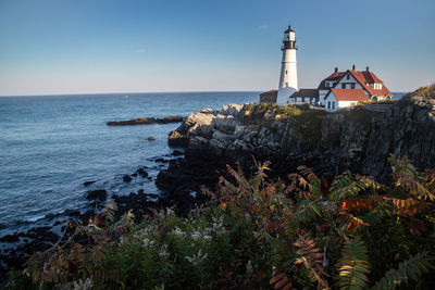 Lighthouse amidst sea and buildings against sky