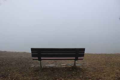 Empty bench on field against sky