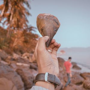 Midsection of person holding rock against sky